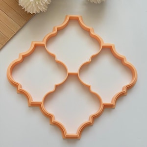 Könnte beinhalten: Ein orangefarbener Ausstecher aus Kunststoff in einem Vierpass-Fliesenmuster. Der Ausstecher besteht aus einem einzigen Kunststoffteil und hat eine glatte Oberfläche. Das Design ist ein sich wiederholendes Muster aus vier abgerundeten Lappen.