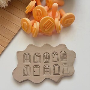 May include: A collection of orange door-shaped stamps and a clay impression. The stamps have handles and various door designs. The clay shows detailed impressions of different door styles, perfect for crafting or artistic projects.