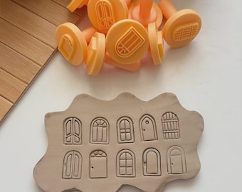 May include: A collection of orange door-shaped stamps and a clay impression. The stamps have handles and various door designs. The clay shows detailed impressions of different door styles, perfect for crafting or artistic projects.