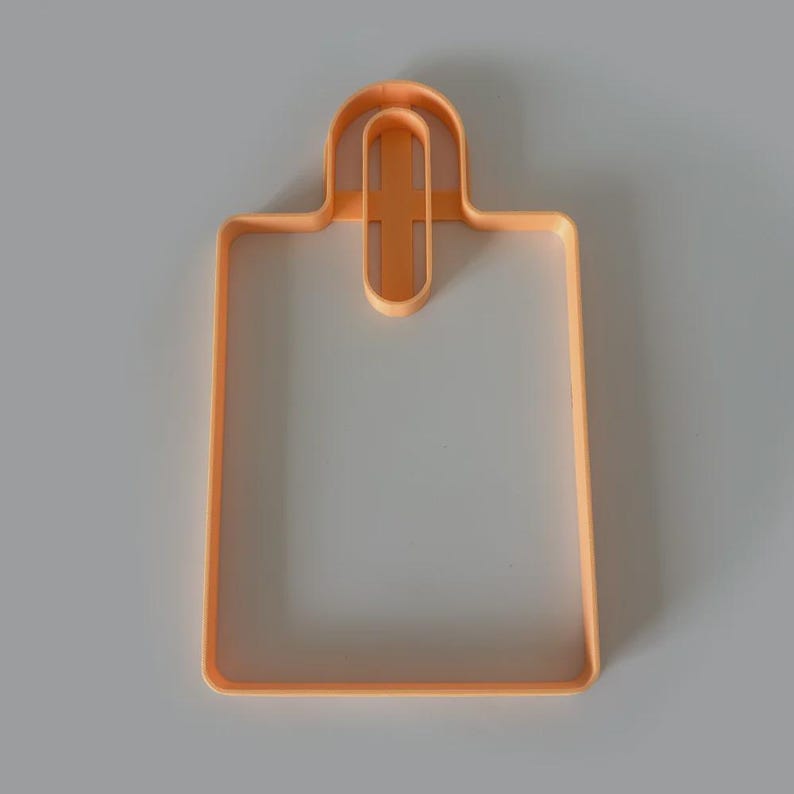 May include: An orange plastic cookie cutter in the shape of a shopping bag. The cutter has a rectangular body with a handle at the top. The design is simple and clean, perfect for baking.