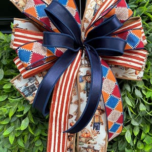 May include: A decorative bow made of multiple ribbons featuring a pattern of scarecrows, pumpkins, and wheat, combined with ribbons in solid navy blue, red and white stripes, and a multi-colored diamond argyle print with blue, orange, and red.