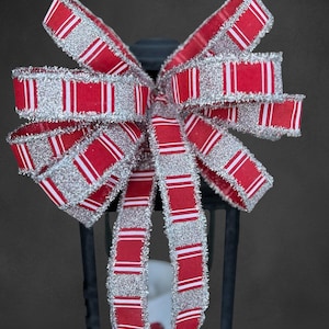May include: A decorative bow with red and white striped ribbon and silver glitter trim. The bow is tied and attached to a black lantern. The bow is a festive decoration.