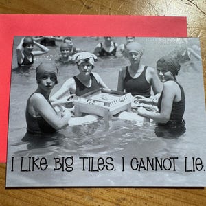 May include: Black and white vintage postcard featuring women in swimsuits playing a game in the water. The text "I LIKE BIG TILES. I CANNOT LIE." is printed at the bottom of the card. The postcard is on top of a red envelope.