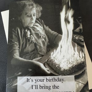 May include: Black and white birthday card featuring a vintage image of a woman holding a cake engulfed in flames. Text on the card reads, "It's your birthday. I'll bring the FIRE EXTINGUISHER!"