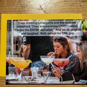 May include: A greeting card with a yellow border features a photo of people at a table with drinks. The card has text that reads, "I was drinking a margarita and the waitress screamed, 'Does anyone know CPR?' I yelled, 'I know the ENTIRE alphabet!'"
