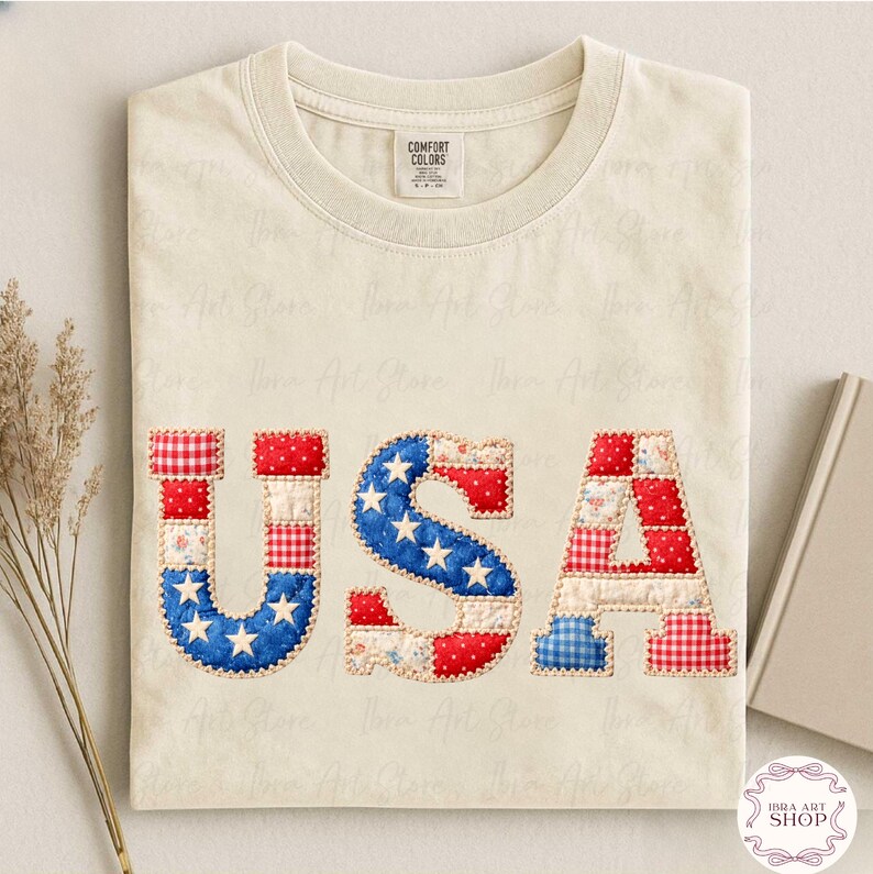 May include: A cream-coloured t-shirt with the word "USA" appliqu&eacute;d across the front. The letters are made of red, white, and blue fabric patches, with the "S" featuring a blue star pattern. The shirt has a crew neck and a tag that says "Comfort Colors".