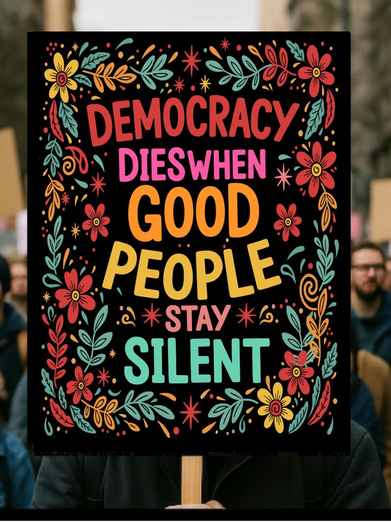 以下が含まれることがあります： 「DEMOCRACY DIES WHEN GOOD PEOPLE STAY SILENT」とカラフルな文字で書かれた黒い看板。赤、黄色、ターコイズ色の花と葉のデザインで装飾されています。木製の棒で支えられています。