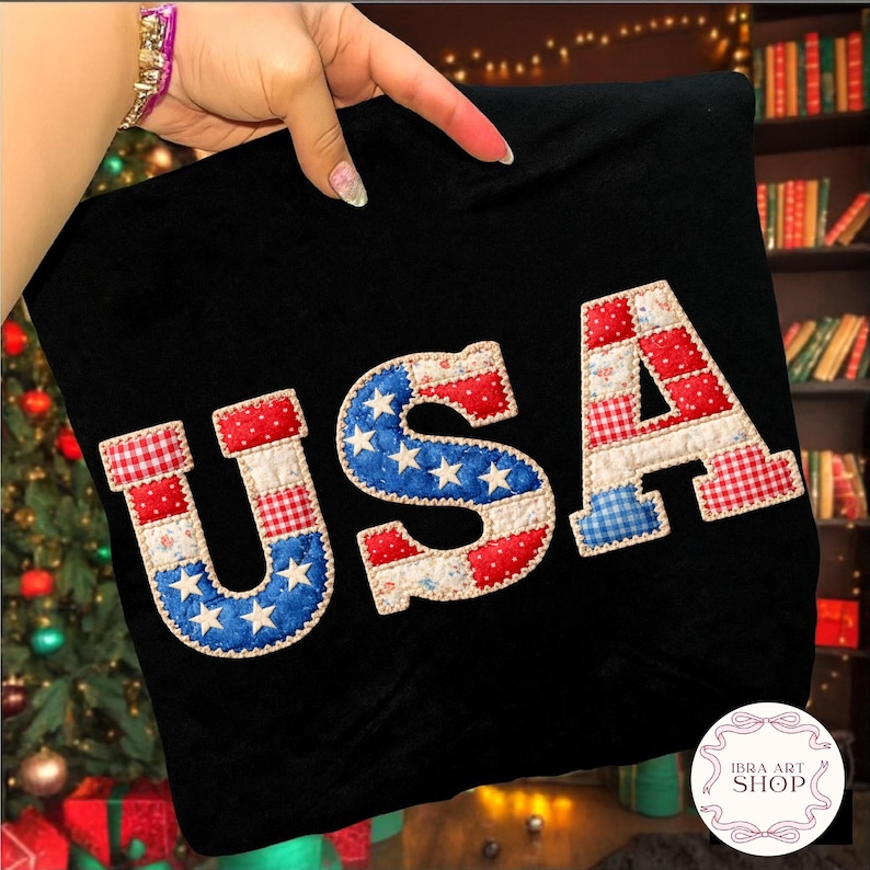 May include: Black fabric with the word "USA" appliqued in red, white, and blue patchwork. The letters are in a patriotic design with stars and gingham patterns. The image is of a decorative item.
