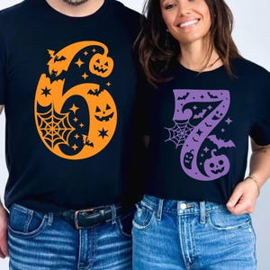Könnte beinhalten: Zwei schwarze T-Shirts mit Halloween-Designs. Eines zeigt die orangefarbene Zahl sechs mit Fledermäusen, Sternen, einem Spinnennetz und einem Kürbis. Das andere zeigt die lila Zahl sieben mit ähnlichen Halloween-Elementen.