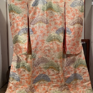 May include: A traditional Japanese kimono in a soft peach colour, adorned with a pattern of stylized fans and floral motifs in shades of blue, green, and purple. The kimono features a red lining and a pink hem.