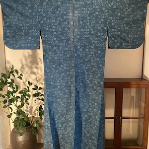 Puede incluir: Un kimono de color verde azulado con un patrón floral repetido. El kimono se muestra abierto, mostrando toda su longitud y mangas anchas. La tela parece ligera, con un brillo sutil. La prenda es una túnica tradicional japonesa.