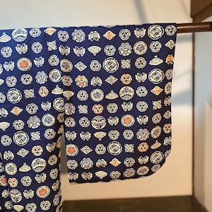 May include: A navy blue kimono with a repeating pattern of white, orange, and cream-colored circular and butterfly designs. The kimono is hanging on a brown rod, showcasing the intricate details of the fabric.