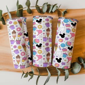 May include: Three cylindrical tumblers with a white background featuring a repeating pattern of colorful cartoon icons including ice cream cones, donuts, coffee cups, and black Mickey Mouse head silhouettes with pink and yellow accents.