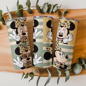May include: Three cylindrical tumblers featuring a repeating pattern of a cartoon mouse character with a polka-dot bow. The design includes horizontal stripes in shades of sage green and tan, with the character making various hand gestures.