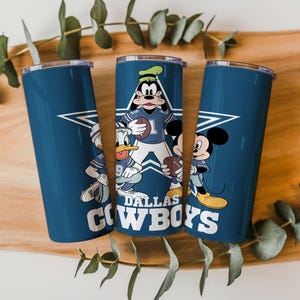 May include: Three cylindrical tumblers with lids featuring a dark blue background, a large white star, and the text DALLAS COWBOYS. The design includes cartoon characters Goofy, Donald Duck, and Mickey Mouse wearing football jerseys and holding footballs.