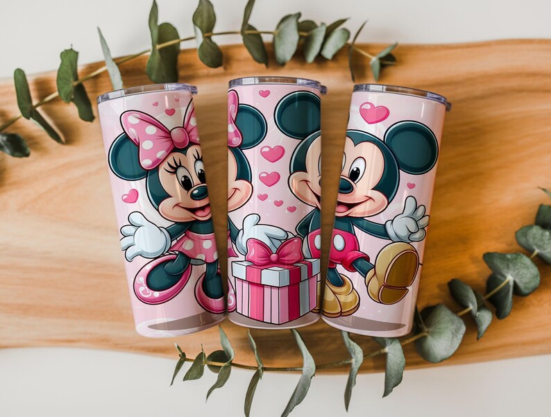 May include: Three cylindrical tumblers with a light pink background featuring cartoon illustrations of Minnie and Mickey Mouse. The design includes small pink hearts, a gift box with a pink bow, and the characters waving, all in a vibrant color palette.