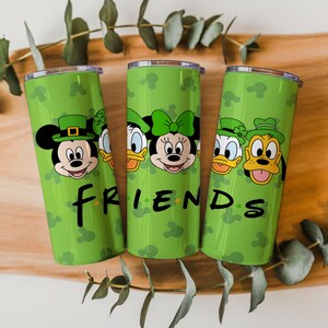 May include: Three cylindrical green tumblers featuring a repeating pattern of Mickey Mouse silhouettes and illustrations of Disney characters wearing green hats. The word FRIENDS is printed in black lettering across the front of the tumblers.
