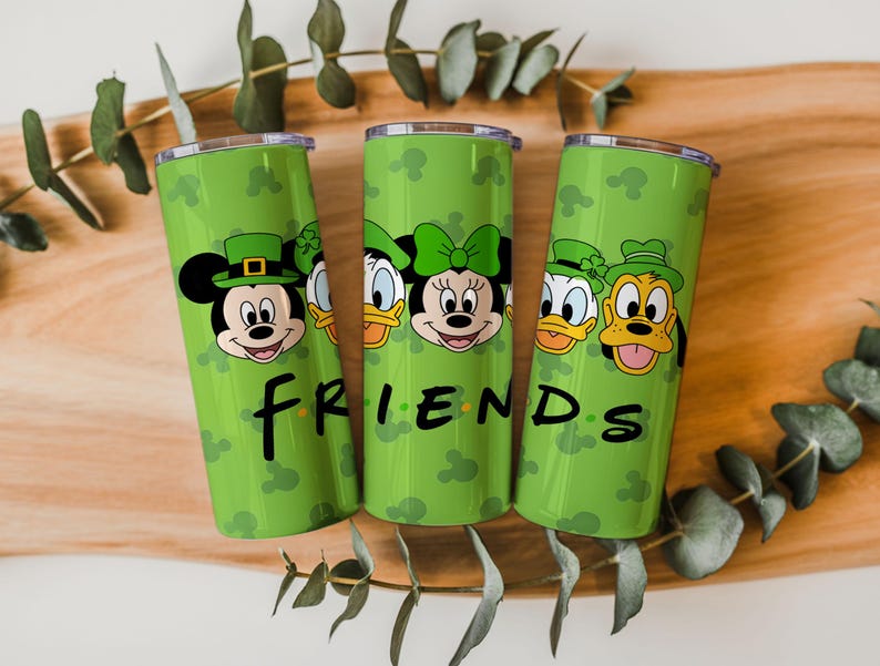 May include: Three cylindrical green tumblers featuring a repeating pattern of Mickey Mouse silhouettes and illustrations of Disney characters wearing green hats. The word FRIENDS is printed in black lettering across the front of the tumblers.