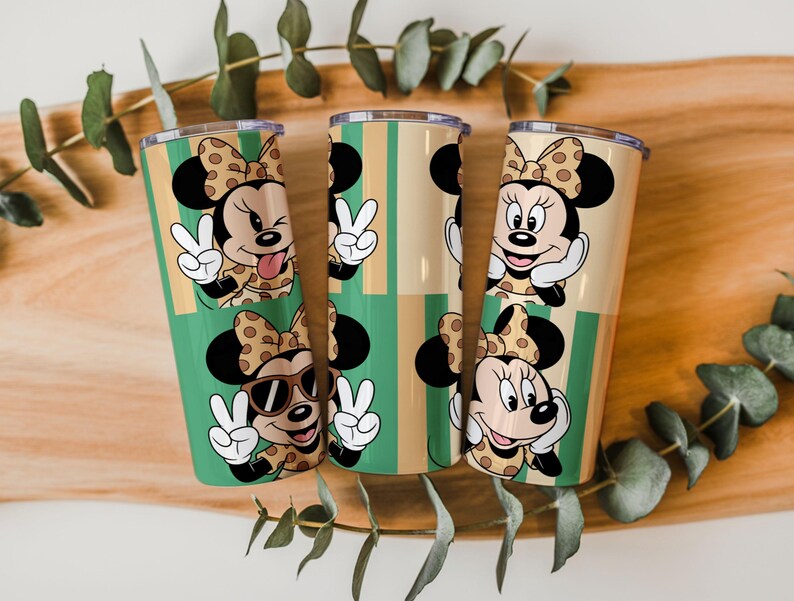 May include: Three cylindrical tumblers featuring a repeating pattern of Minnie Mouse characters. The design includes Minnie with a polka dot bow, making peace signs, wearing sunglasses, and winking, set against a background of vertical green and tan stripes.