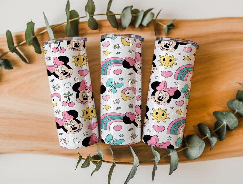 May include: Three cylindrical tumblers with a white background featuring a repeating pattern of Minnie Mouse faces with pink bows, yellow suns, rainbows, blue butterflies, white daisies, pink hearts, and red cherries with green stems.