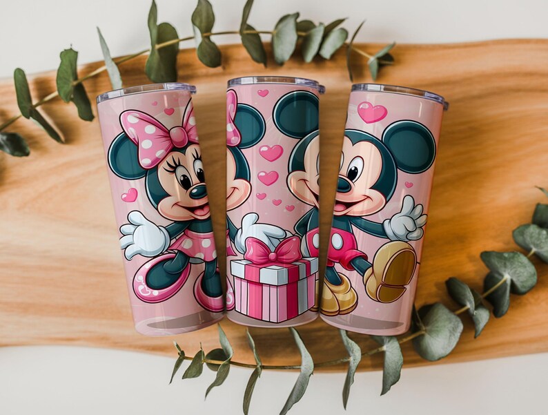 May include: Three cylindrical tumblers with a light pink background featuring cartoon characters Minnie and Mickey Mouse. The design includes pink hearts, a gift box with a pink bow, and the characters in their classic outfits with white gloves.