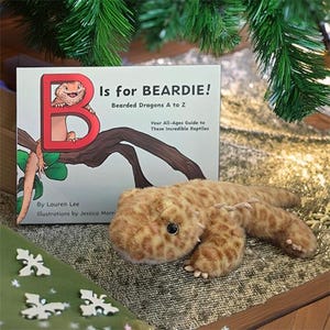 May include: A children's book titled "B is for Beardie! Bearded Dragons A to Z" with a plush bearded dragon toy. The book cover features a red "B" with a cartoon bearded dragon. The plush toy is brown with yellow spots.