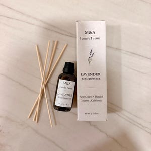 May include: A brown glass bottle with a black cap and a white rectangular box, both labeled M&A Family Farms Lavender Reed Diffuser 60 ml | 2 fl oz, accompanied by five thin, light-colored wooden reeds for fragrance diffusion.