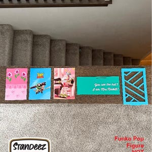 May include: A collection of colorful cards and a blue geometric cutout are displayed on a wooden surface. The cards feature floral designs, Toy Story characters, and the text "You see the hat? I am Mrs. Nesbitt!" A "Standeez" sticker is also present.