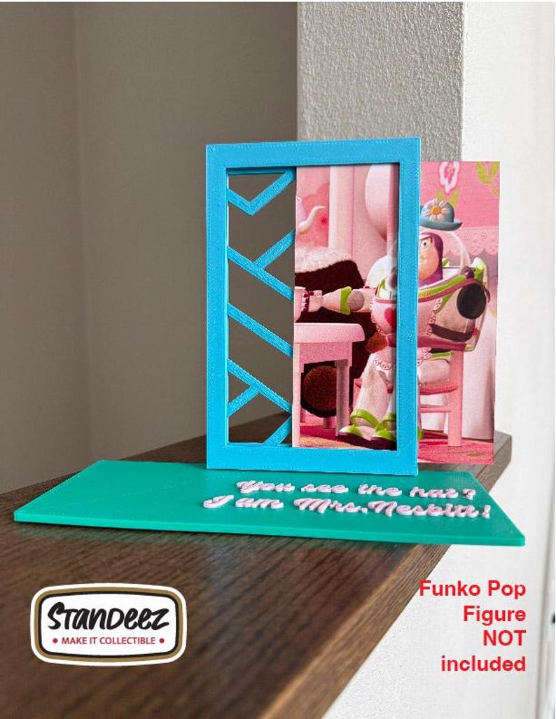 May include: A teal display stand with a blue frame and a printed image of a character. The stand has the text "You see the hat? I am Mrs. Nesbitt!" The Funko Pop figure is not included.