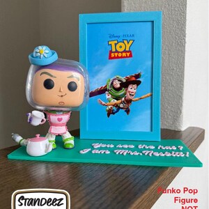 May include: A Funko Pop figure of Buzz Lightyear in a Mrs. Nesbit costume, holding a teacup, with a blue picture frame featuring a Toy Story movie poster. The base is green with the text "You see the hat? I am Mrs. Nesbit!"