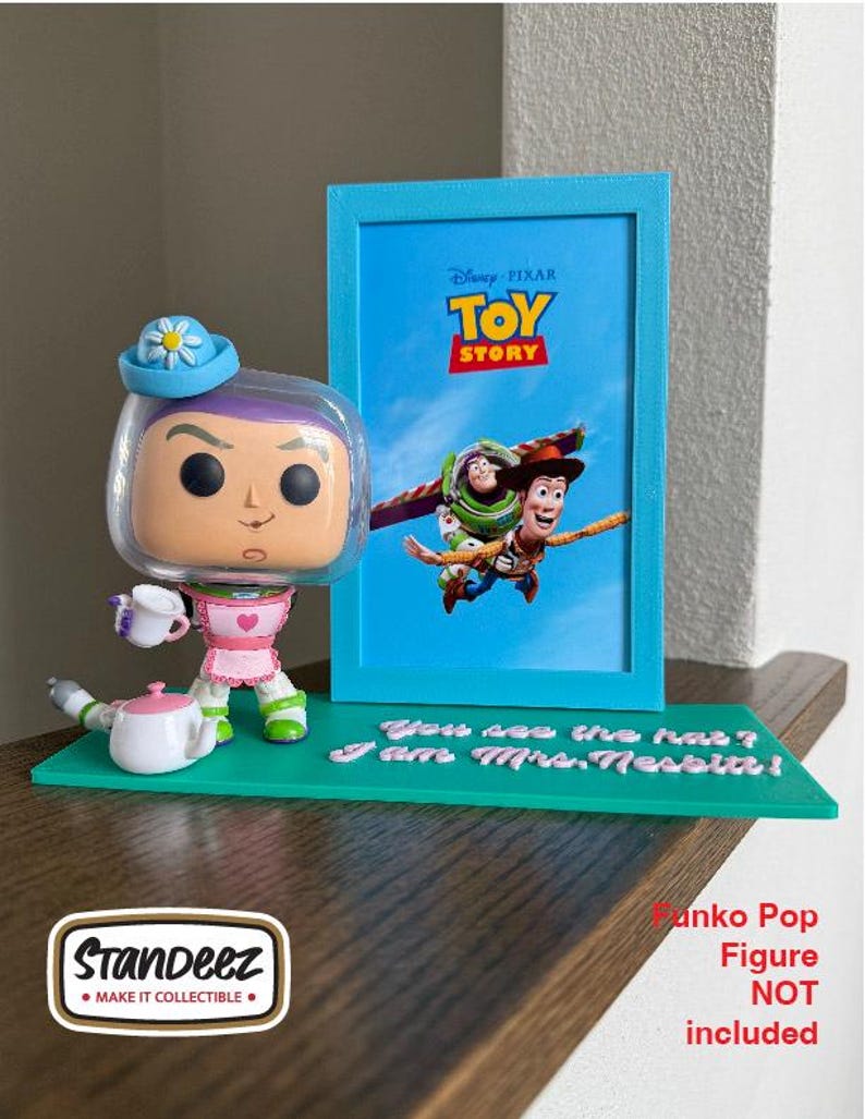 May include: A Funko Pop figure of Buzz Lightyear in a Mrs. Nesbit costume, holding a teacup, with a blue picture frame featuring a Toy Story movie poster. The base is green with the text "You see the hat? I am Mrs. Nesbit!"