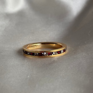 May include: A gold band ring with a row of red and white gemstones.