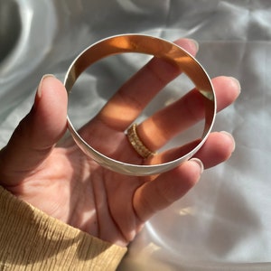 May include: A silver bangle bracelet with a polished finish. The bracelet is open and has a slightly rounded shape.