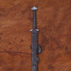 May include: A dark brown sword in a sheath, with a silver-colored pommel and tip. The handle is wrapped in a spiral pattern. The sheath is secured with leather straps. The background is a textured brown surface.