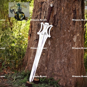 Pu&ograve; includere: Una spada in metallo color argento con un'impugnatura avvolta in marrone scuro e una guardia dalla forma distintiva. La lama presenta una cresta centrale e una punta affilata. Un piccolo grafico di un cavaliere con un'ascia &egrave; visibile in alto.