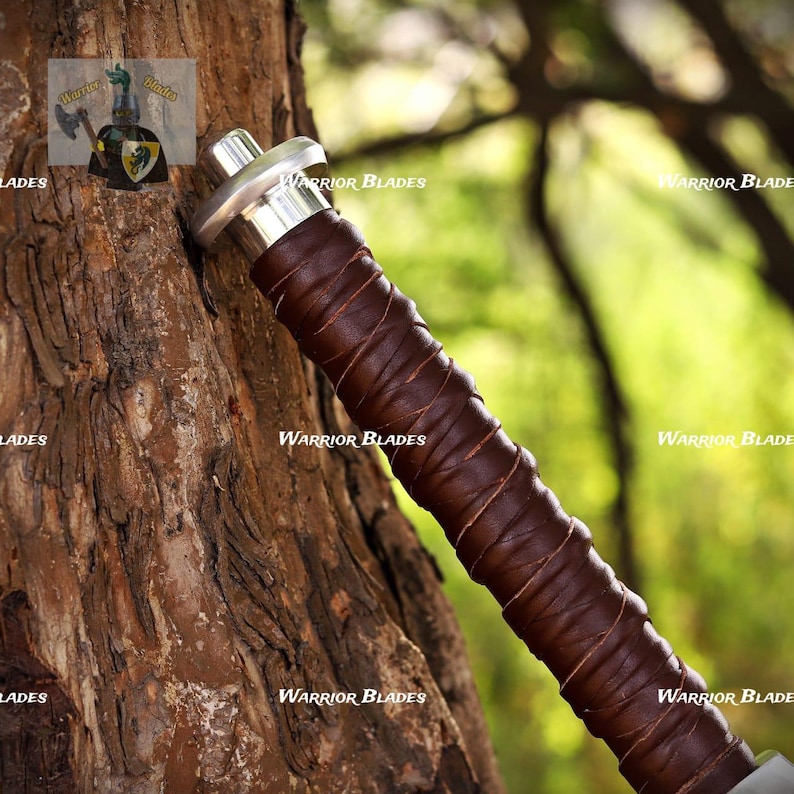 Pu&ograve; includere: Un'impugnatura di spada con presa rivestita in pelle marrone scuro e un pomolo in metallo color argento sulla parte superiore. L'impugnatura &egrave; caratterizzata da strisce di pelle sovrapposte. Il testo Warrior Blades &egrave; visibile pi&ugrave; volte.