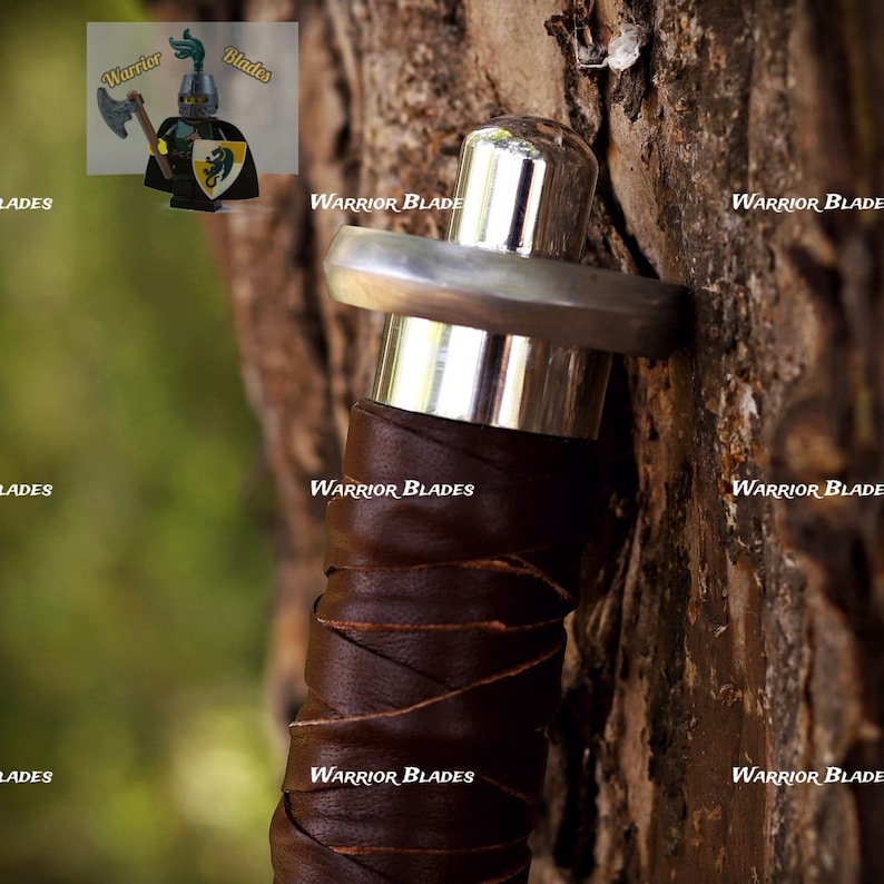 Pu&ograve; includere: Un'impugnatura di spada con un'impugnatura rivestita in pelle marrone scuro, una guardia in metallo color argento lucido e un pomolo arrotondato. Il testo Warrior Blades &egrave; visibile pi&ugrave; volte nell'immagine, insieme a una piccola figura di cavaliere.