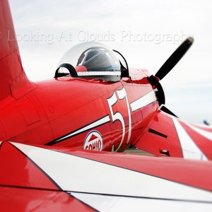 May include: A red and white airplane with the number 51 on the side. The airplane has a propeller and a cockpit. The airplane is painted with a white stripe and the word "Sohio" on the side.