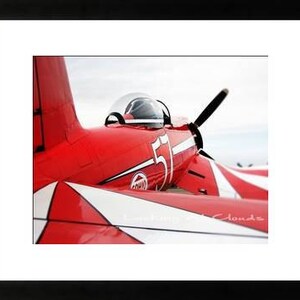 May include: A red and white airplane with the number 51 on the side. The plane is in flight and the sky is blue.