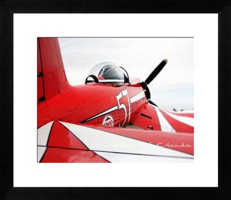 May include: A red and white airplane with the number 51 on the side. The plane is in flight and the sky is blue.