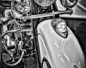 May include: A black and white photo of a vintage motorcycle with a chrome headlight and a chrome fender. The motorcycle has a chrome Indian head emblem on the front fender.