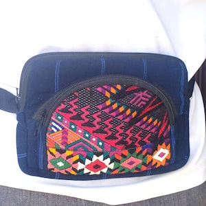 May include: A navy blue fanny pack with a colorful, patterned front pocket. The pocket features a geometric design with red, pink, green, and yellow accents. The pack has a black zipper and a navy blue adjustable strap.
