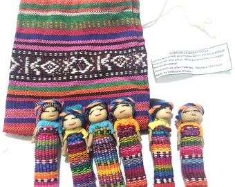 Könnte beinhalten: Sechs kleine Puppen mit garnumwickelten Körpern und Outfits aus buntem Webstoff, angeordnet vor einem passenden Beutel mit Kordelzug. Ein kleines weißes Papieretikett enthält den Text GUATEMALA WORRY DOLLS und beschreibende Informationen.