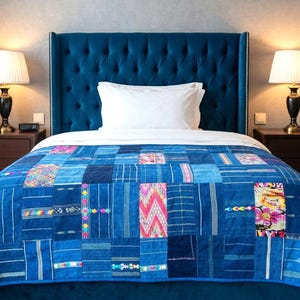 May include: A bed featuring a tall, tufted, deep blue velvet headboard and a patchwork quilt composed of various blue fabric rectangles, some with intricate woven patterns, colourful floral embroidery, and geometric designs in pink and yellow.