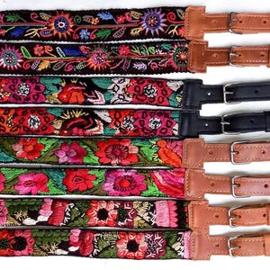 Könnte beinhalten: Sieben bestickte Taschenriemen mit farbenfrohen Blumenmustern. Jeder Riemen zeigt ein anderes Design mit Farben wie Rot, Rosa, Grün und Blau. Die Riemen sind mit Leder und Metallbeschlägen versehen.