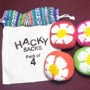 May include: A set of four hacky sacks with a canvas bag. The hacky sacks are red, pink, orange, and green, each with a white flower design and a yellow center. The bag is white with the words "HACKY SACKS Pack of 4".