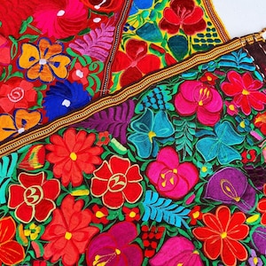 Puede incluir: Primer plano de textiles bordados vibrantes con una variedad de flores coloridas. Los textiles muestran una rica paleta de rojos, rosas, azules y morados, con costuras intrincadas y un borde con flecos.