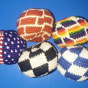 May include: Five colorful crocheted hacky sacks. One features the American flag design, while others have brick, rainbow, checkerboard, and blue and white diamond patterns. These handmade footbags are perfect for juggling and outdoor games.