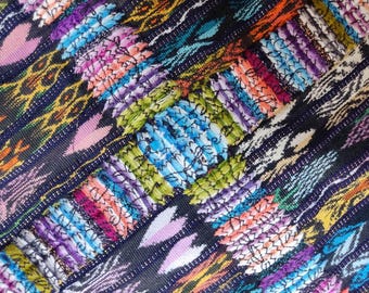 Puede incluir: Primer plano de un textil tejido con un patrón complejo. La tela presenta un fondo azul oscuro con rayas diagonales y detalles bordados coloridos. El bordado incluye tonos de rosa, azul, verde, naranja y morado, creando un diseño vibrante y texturizado.