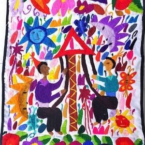 May include: Embroidered textile art with a white background, featuring colorful figures and floral designs. The artwork includes two figures, a red triangle, suns, and various flowers in shades of blue, orange, purple, and green. The border is black.